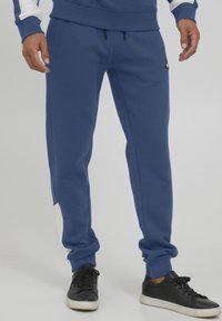 Blue sweatpants in cotton blend material; tapered fit with an elastic waistband, featuring a white accent on the side and adjustable drawstrings.