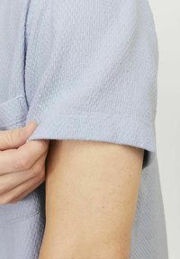 Lichtblauw shirt met korte mouwen, gemaakt van textuurstof met een hexagonaal patroon, met een relaxte pasvorm en zichtbare stiksels.