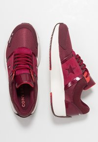 Burgundowe sportowe sneakersy z siateczkowego materiału, z błyszczącymi akcentami, logo w kształcie gwiazdy oraz białą podeszwą. Posiadają teksturowane nakładki oraz kontrastowe sznurowadła.