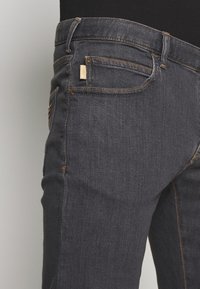 Dark denim jeans with a slim fit, featuring orange stitching and a small label on the back pocket. Smooth texture and classic design.