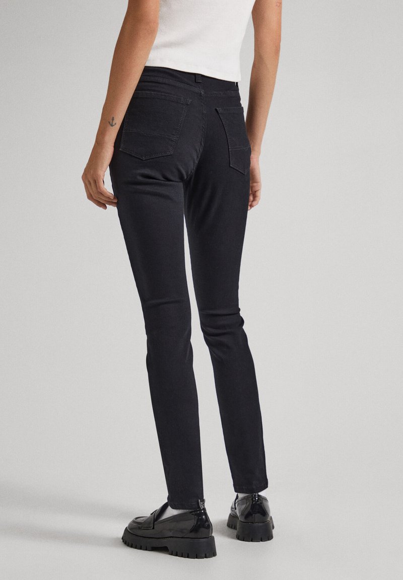 Schwarze enge Jeans aus Denim mit mittelhohem Bund, zwei Gesäßtaschen und glatter Textur. Getragen mit schwarzen klobigen Schuhen.