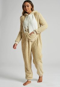 Beige, fluffy onesie met een wit paneel waarop een klein geborduurd dierengezichtje staat. Lange mouwen en elastische manchetten, inclusief een voorzak.