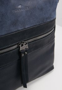 Marineblauwe en zwarte leren rugzak met gladde en gestructureerde oppervlakken, voorzien van een voorste ritszak en ritsaccentdetails.