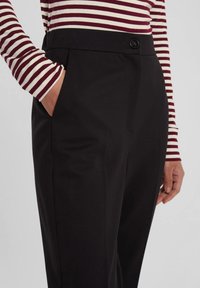 Pantaloni neri su misura con una texture liscia, dotati di chiusura a bottone e tasche laterali. Abbinati a un top a righe con maniche lunghe.
