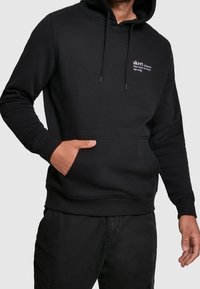 Felpa nera con cappuccio in tessuto dalla texture liscia, con tasca frontale, coulisse e scritta bianca sul petto. Abbinabile a pantaloni neri.