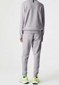 Šedá mikina a tepláky s žebrovanými manžetami, hladkou texturou a zeleným akcentem na zádech. Nošeno se světle zelenými teniskami.