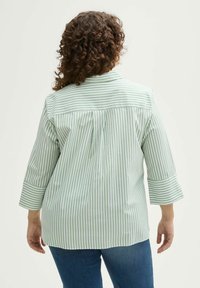 Camicia a righe verde chiaro e bianca, con colletto, maniche a tre quarti e dettaglio a pieghe sul retro. Indossata con jeans blu.
