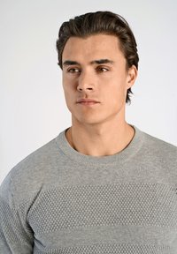 Ljust grå stickad tröja med strukturerade horisontella ränder och ribbad rund halsringning. Har en mjuk finish och tyg med medelvikt.