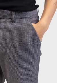 Szare spodnie w wzory z teksturowanym splotem, z bocznymi kieszeniami i średnim stanem w pasie. Szczegóły obejmują szlufki na pasek oraz dopasowany krój.