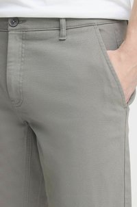 Pantalon gris clair en tissu lisse, avec un design de poche classique et une fermeture à bouton à la taille.
