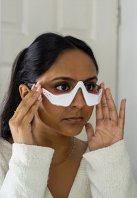 Białe sportowe gogle z czerwonymi wykończeniami i eleganckim, kanciastym designem. Noszone na twarzy, z widocznymi rękami dostosowującymi oprawki.