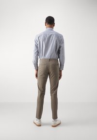 Pruhovaná modro-bílá košile na knoflíky spárovaná s úzkými béžovými kalhotami a bílými teniskami; má zadní kapsy a texturovanou látku.