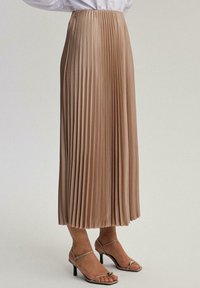 Pleated midi-hame vaaleasta beige-kankaasta, jossa on korkea joustava vyötärö ja virtaava rakenne, yhdistettynä remmikenkiin, jotka ovat myös beige.