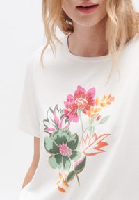 Camiseta de algodón blanca con un diseño floral en tonos de rosa, naranja, verde y amarillo, con cuello redondo y mangas cortas.