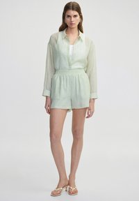 Camisa de lino verde claro con mangas largas, abotonada, combinada con pantalones cortos a juego con una cinturilla elástica. Diseño y textura simples.