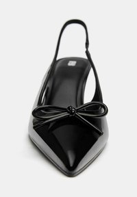 Čierne lakované slingback topánky s špicatou špičkou a mašľou, majúce hladký povrch a štíhly podpätok pre elegantný dizajn.