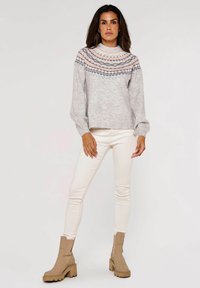 Hellgrauer Strickpullover mit gemustertem Yoke in Pink und Blau, kombiniert mit cremefarbenen Skinny Jeans und beigen Stiefeletten.