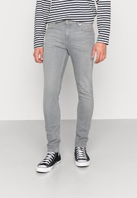 Jeans de mezclilla gris con un ajuste slim, que cuentan con un diseño clásico de cinco bolsillos, un desvanecido sutil y una cintura de talle medio, combinados con zapatillas negras.