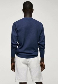 Navy blue knitted sweater with long sleeves, ribbed cuffs, and neckline. Worn with white linen shorts for a light, casual look.