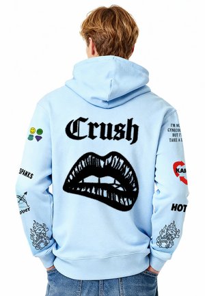 Felpa con cappuccio azzurro chiaro con una grande grafica nera a forma di labbra e la scritta "Crush". Include varie toppe colorate e testi sulle maniche. Tessuto confortevole.