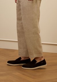 Zwarte suède instap schoenen met een witte rubberen zool, gedragen met lichtbeige linnen broeken, die een casual, minimalistisch ontwerp laten zien.