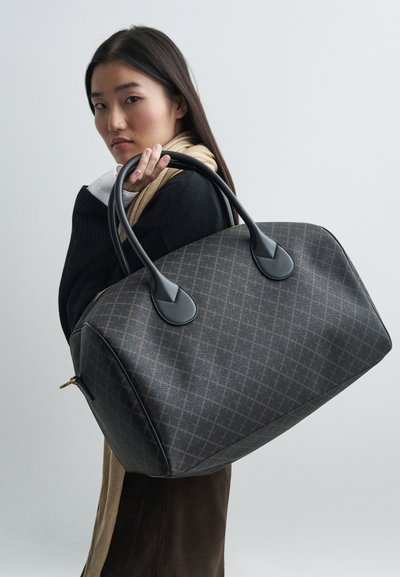 Velká, strukturovaná hnědá taška s diamantovým vzorem, černými koženými držadly a zlatým zipem. Hladký povrch s jemnými detaily.