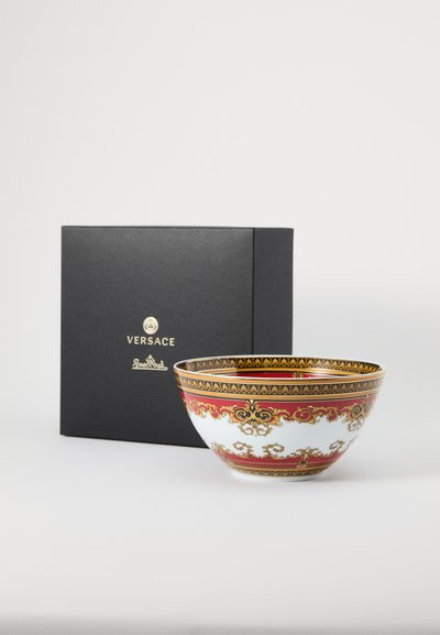 Κεραμικό μπολ με λευκό σώμα, διακοσμητικά κόκκινα και χρυσά μοτίβα, και παχύ χρυσό χείλος, δίπλα σε μαύρο κουτί Versace με λογότυπο.
