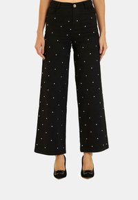 Pantaloni a gamba larga neri in denim, decorati con pois bianchi. Presentano tasche e una chiusura con bottone, abbinati a scarpe con tacco nere.