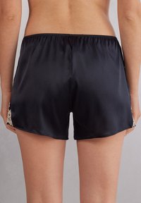 Zwarte satijnen korte broek met een glanzende textuur, voorzien van delicate kanten details aan de zijkanten en een elastische tailleband voor comfort.
