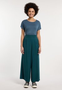 Top blu textured casual abbinato a pantaloni larghi teal e sneakers nere alte. Design minimalista con dettagli sottili.