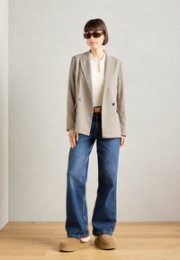 Blazer a scacchi beige e marrone, top bianco a coste, jeans blu a vita alta e scarpe con zeppa color beige con trim in pelliccia. Occhiali da sole marroni.