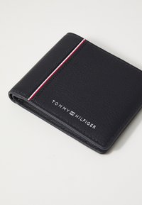 Billetera de cuero navy con un acabado texturizado, que presenta un acento de rayas rojas y blancas y el logo en relieve "TOMMY HILFIGER" en el frente.