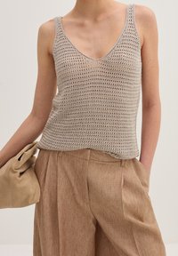 Top in maglia beige senza maniche con scollatura a V e spalline sottili, caratterizzato da un motivo a trama aperta. Abbinato a pantaloni beige a vita alta con texture e una pochette.