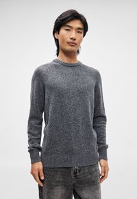 Pulover tricotat de culoare gri închis, cu guler rotund, manșete cu model în relief și o textură ușor presărată, asortat cu blugi negri. Design simplu și clasic.