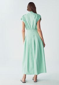 Mäta zelená, šaty midi s krátkymi rukávmi, so zúženým pásom, plisovaním a jemným leskom, doplnené neviditeľným zipsom na chrbte.