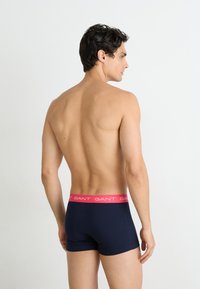 Marineblauwe katoenen boxershort met een roze elastische tailleband met daarop het "GANT" logo, weergegeven gedragen vanuit een zijaanzicht, wat een gladde textuur onthult.