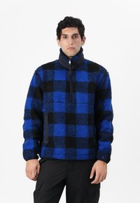 Fleece-pullover i blå og sort ternet mønster, høj krave, halv-lynlås foran og sidelomme med lynlås. Blød tekstur og afslappet pasform.