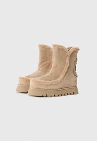 Beige ruskinn ankle boots med faux fur-beskæring, gummisål, dekorativ rhinestone-bånd og en stiliseret accent på siden.
