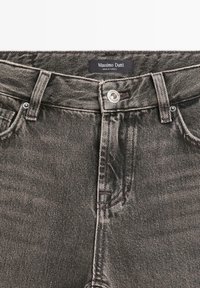 Jeans in denim nero con design aderente. Presentano una chiusura con bottone argento e un'etichetta con marchio vicino alla cintura. Cuciture dettagliate visibili.