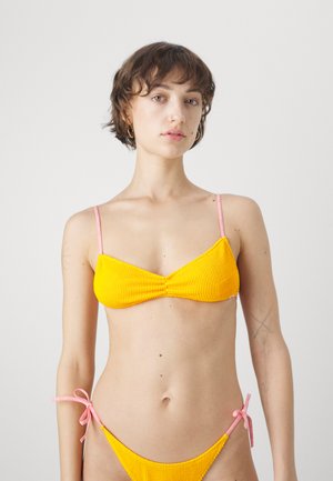Yellow ribbed bikini top with pink straps; bottom has tie details at the sides. Smooth texture, minimalist design, and vibrant color contrast.