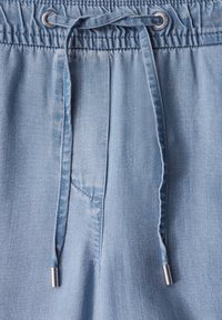 Jasnoniebieskie szorty dżinsowe z elastycznym, marszczonym paskiem w talii oraz sznurkiem do regulacji, zwieńczonym metalowymi końcówkami. Gładka tekstura, minimalne przeszycia.