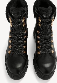 Schwarze Leder-Stiefeletten mit Kunstfutter, ausgestattet mit metallischen goldenen Ösen, schwarz-weißen gesprenkelten Schnürsenkeln und einem robusten Sohlen-Design.