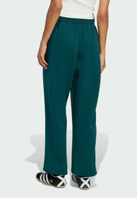 Grønne, højtaljede sweatpants med en afslappet pasform og elastisk talje, lavet af blødt stof. Sorte og hvide atletiksko fuldender looket.