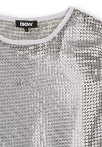 Haut argenté à paillettes avec une bordure blanche autour de l'encolure et une étiquette noire DKNY taille 8 à l'intérieur du col.