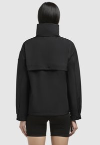 Giacca nera con colletto alto, caratterizzata da un design pulito e spalle strutturate, realizzata in un tessuto morbido, mostrata di spalle.