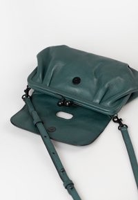 Borsa a tracolla in pelle teal con design plissè, accessori neri, tracolla removibile e chiusura a scatto. L'interno presenta un'apertura funzionale.