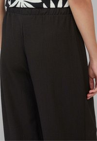 Mörka, texturerade vida byxor med ett mjukt samlat elastiskt midjeband. Ytan har ett subtilt mönster. Enkelt utförande utan extra detaljer.