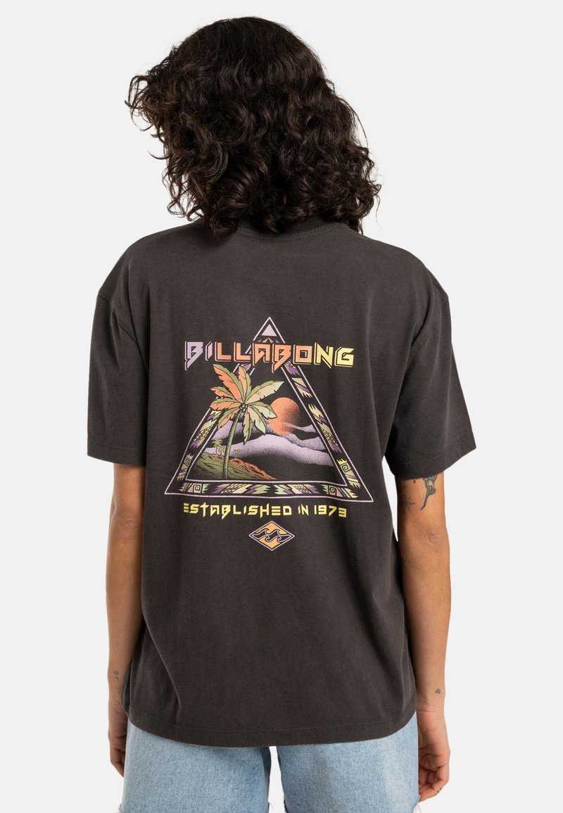 Musta puuvillapaita, jossa on värikäs kolmio grafiikka palmupuiden, vuorten ja auringon kanssa. Takana on tekstit "BILLABONG" ja "Perustettu vuonna 1973."