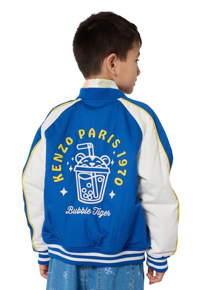 Blauwe en witte bomberjack met geribbelde manchetten, voorzien van een drankgrafiek en tekst op de achterkant, in gele en witte borduursels.