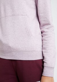 Ljuslila sweatshirt med en känguruficka, ribbade muddar och fåll, och ett mjukt, texturerat tyg. Matchad med mörkmaroonfärgade byxor.